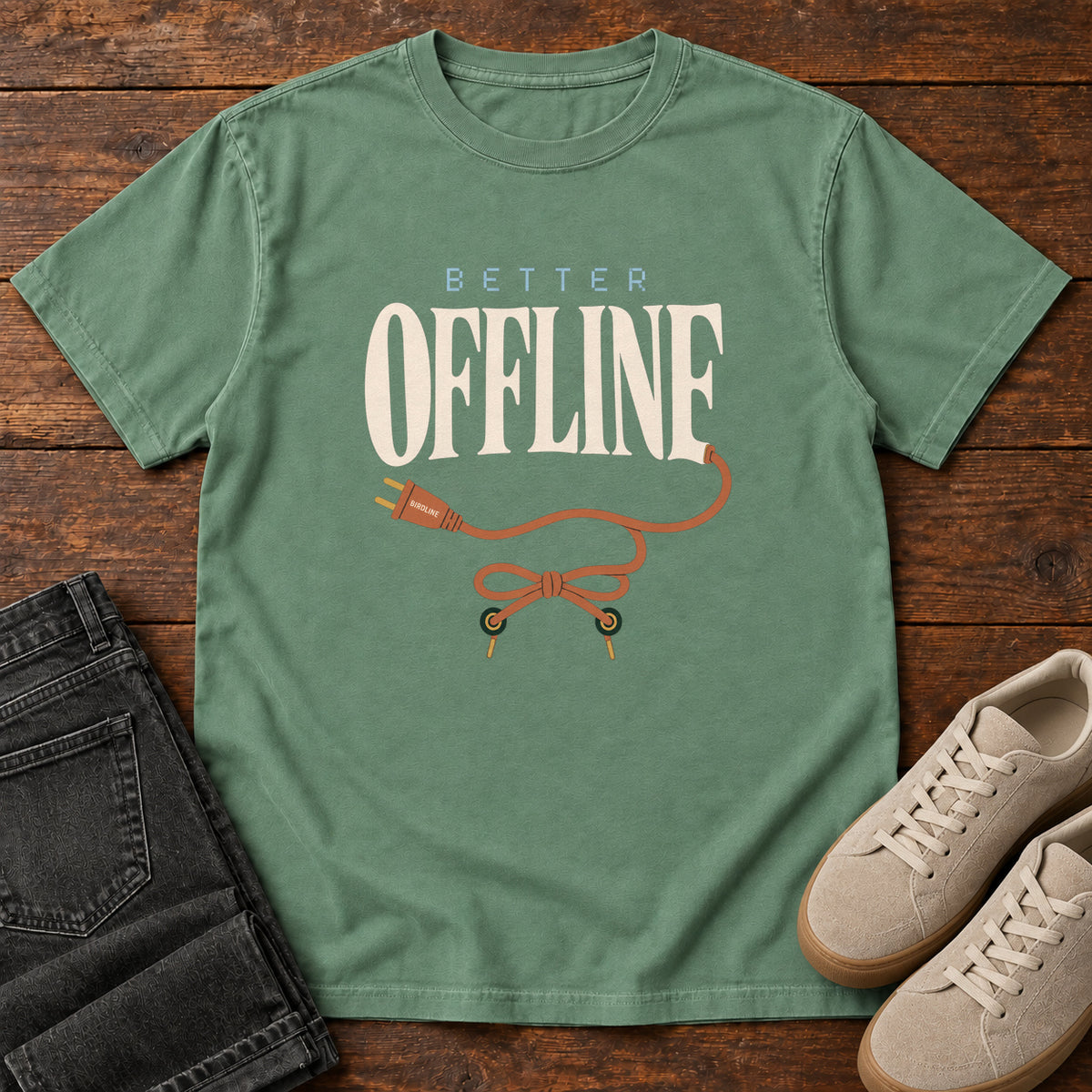 Light Green Better Offline T-Shirt with cream Better Offline lettering and an orange unplugged cord; front flat lay on wood.