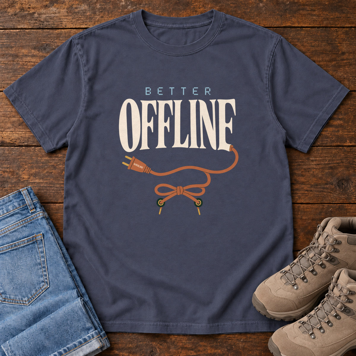 Navy Better Offline T-Shirt with cream Better Offline lettering and an orange unplugged cord; front flat lay on wood.