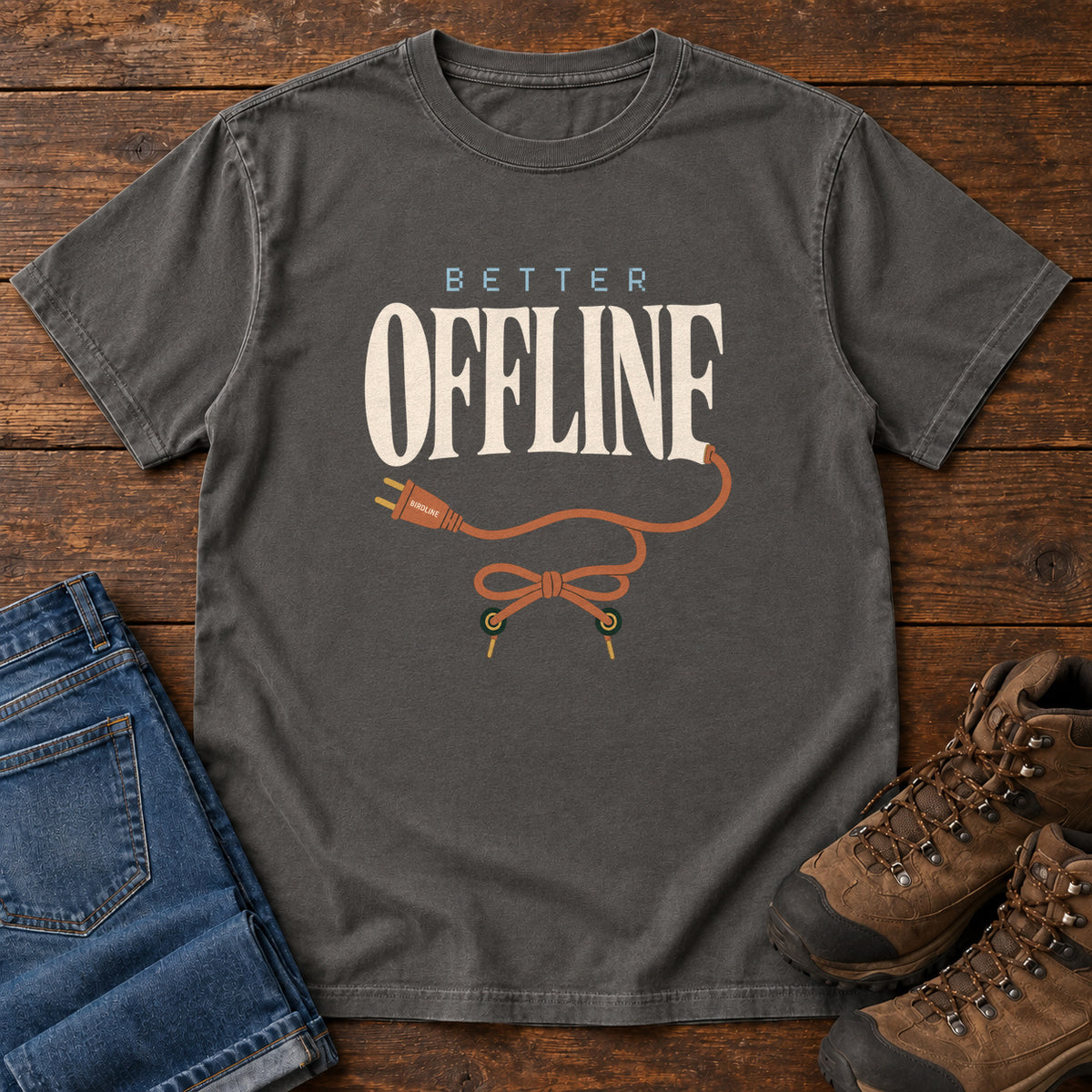 Pepper Better Offline T-Shirt with cream Better Offline lettering and an orange unplugged cord; front flat lay on wood.