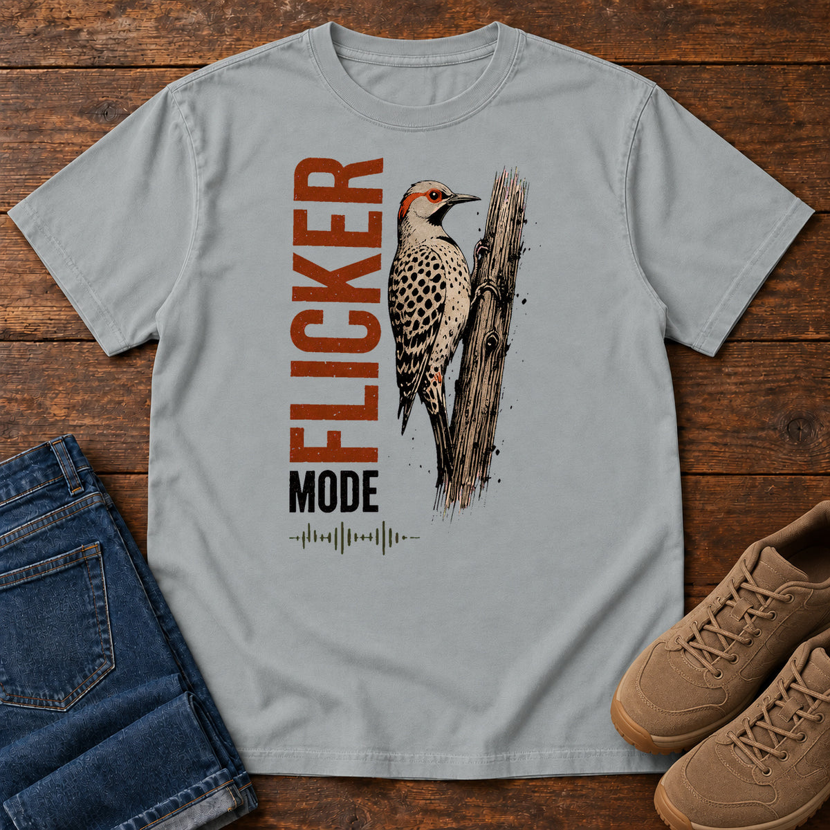 Granite Flicker Mode T-shirt with a spotted bird on a tree trunk and Flicker Mode lettering, laid flat on a wooden surface.