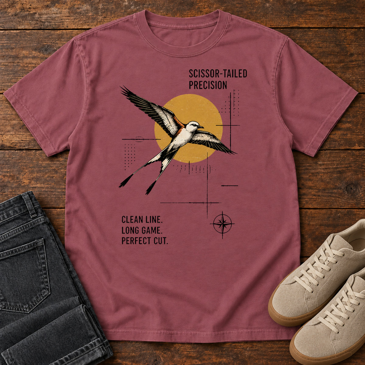 Brick Scissor Tailed Precision T-Shirt with a long, fork-tailed bird in flight over an ochre circle and technical-style linework, front flat lay on wood.